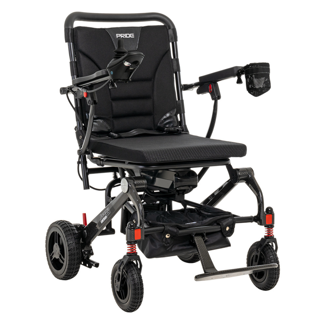 The Pride Mobility Jazzy® Carbon Ultralite Powerchair is a lightweight black electric wheelchair styled with padded seat and armrests, right-side joystick control, large rear and anti-tip front wheels, and a storage pouch—ideal as a travel power chair.